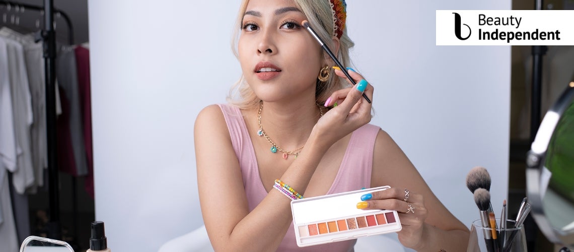 Image of beauty influencer applying eye shadow in front of a white backdrop 