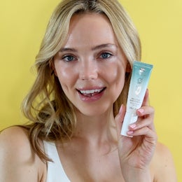 Image of a woman holding a bottle of Age IQ InvisiBloc Sunscreen Gel.