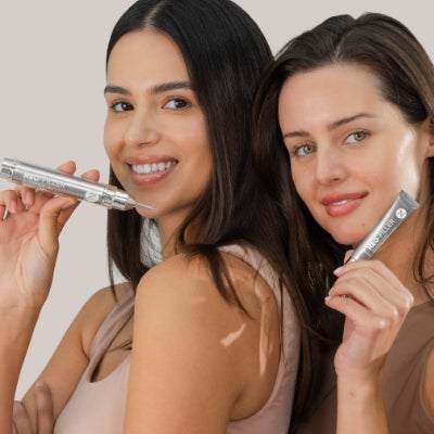 Two women posing with a Neo-FILLER tube and a Neo-FILLER Volumizing Lip Treatment tube.