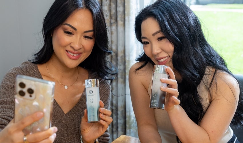 Two women taking a selfie with Age IQ Day & Night Cream bottles.