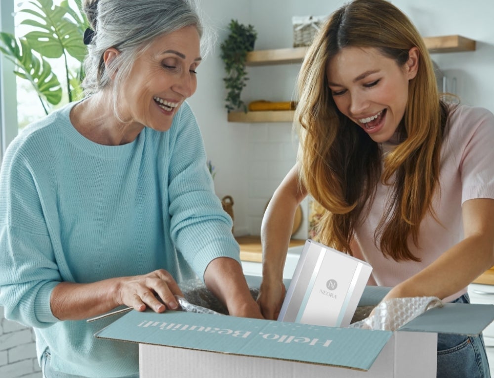 An older woman and daughter opening a Neora branded box filled with items.
