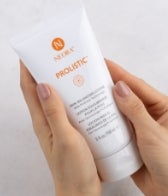Hands holding a tube of Neora's Prolistic Lotion.