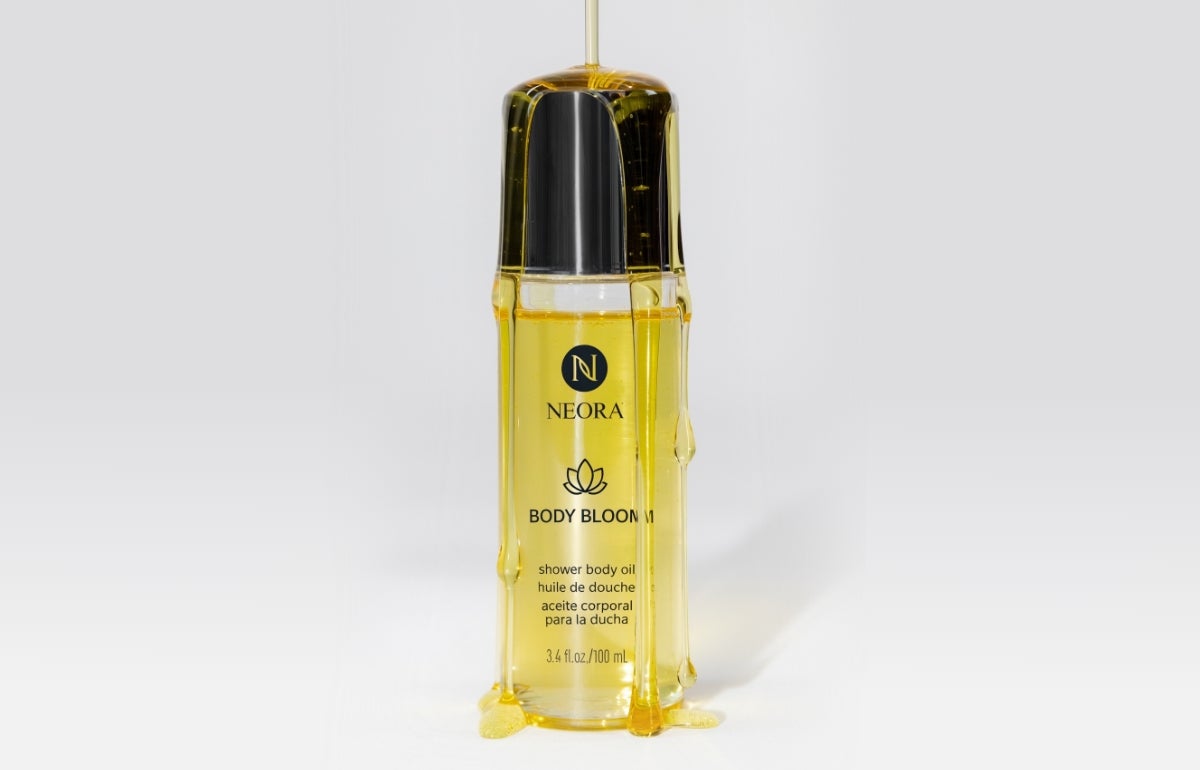 A Neora Body Bloom bottle being drenched in the product’s shower body oil.