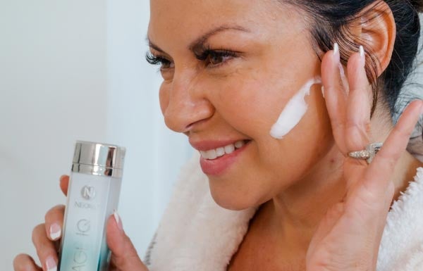 A woman applying Age IQ Day Cream to her face in a bathroom