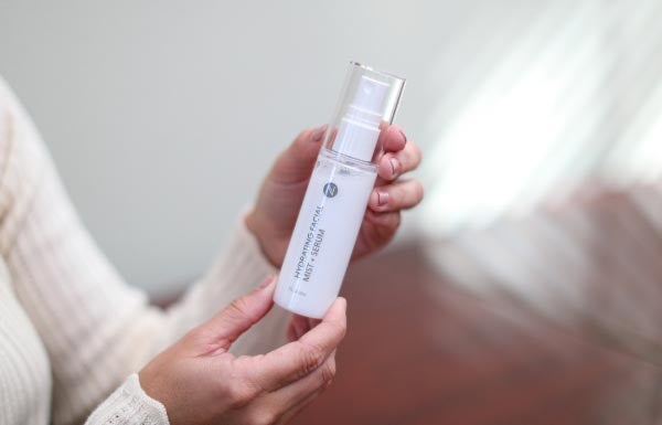 A woman holding up the Hydrating Facial Mist bottle in sunlight.