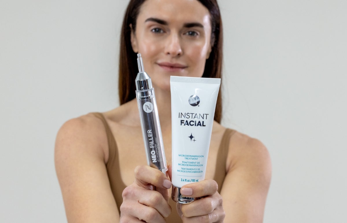 A woman holding a Neo-FILLER tube and Instant Facial tube in front of her body.