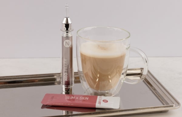 A sachet of Slim + Skin & Neo-FILLER tube displayed next to a glass cup filled with coffee on a metal platter.