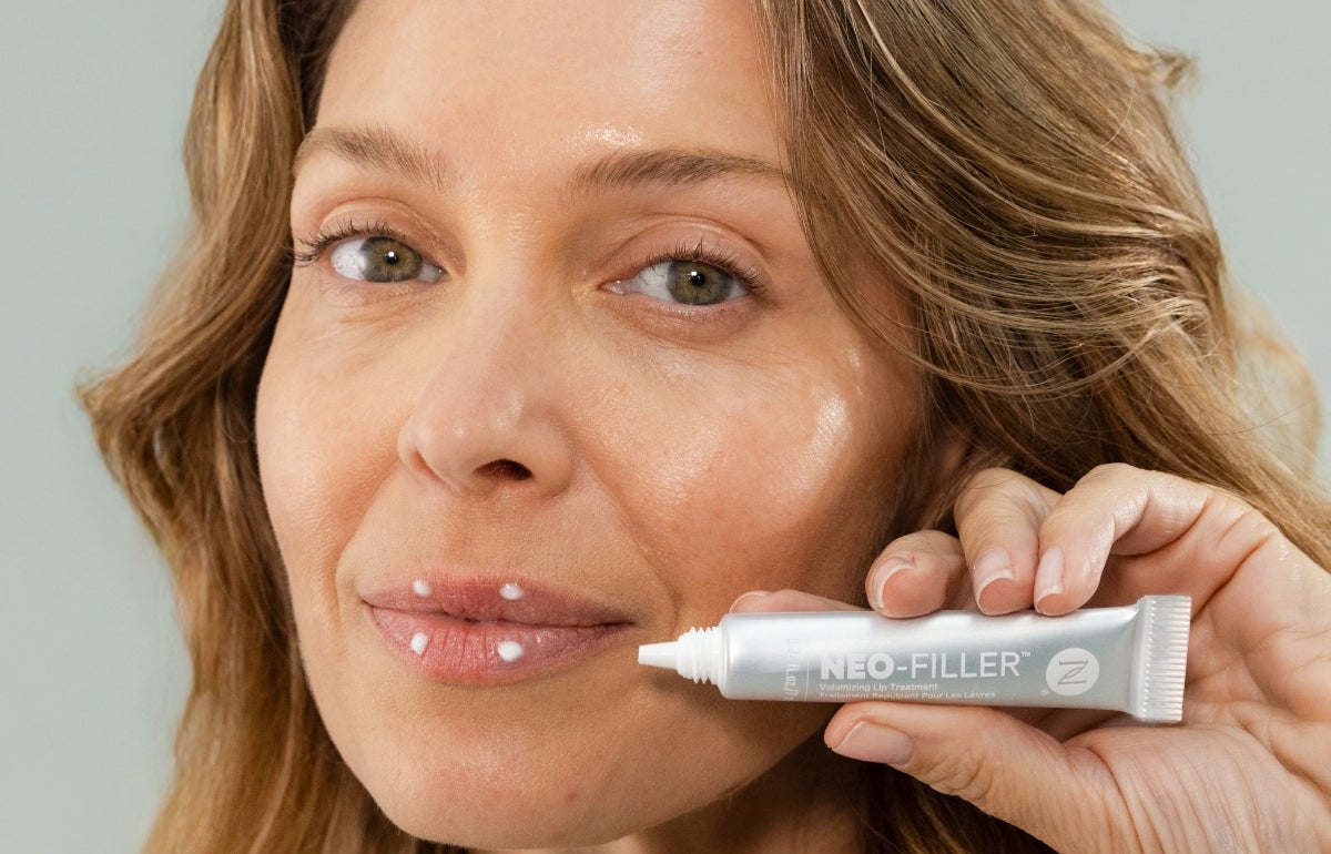 A woman applying Neo-FILLER Volumizing Lip Treatment to her lips.