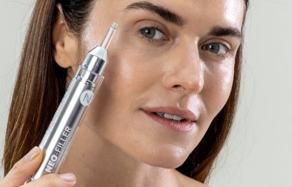 A woman holds up a Neo-FILLER tube next to her face.