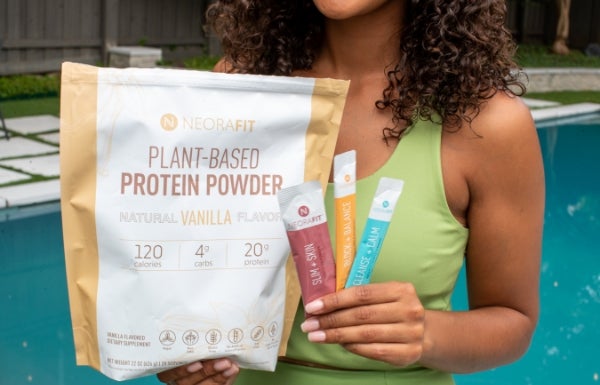 A woman holding up the NeoraFit™ + Protein Powder Starter Set in front of a swimming pool.