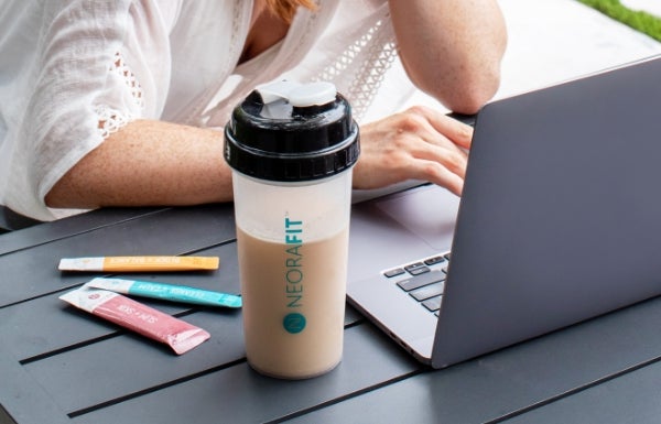 A woman working on her computer with NeoraFit™ + Protein Powder Starter Set next to her.