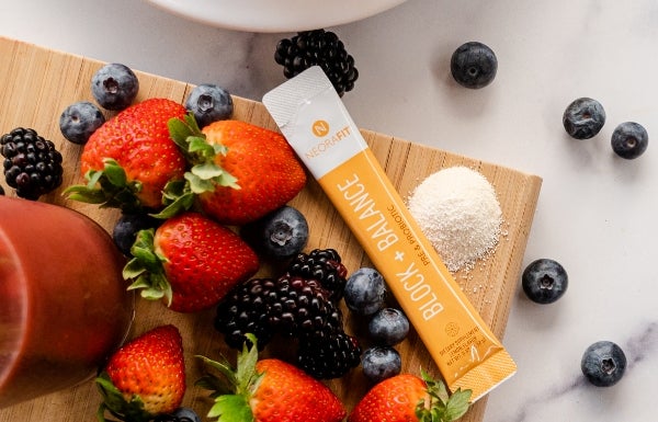 Lifestyle shot of NeoraFit™ Block + Balance Pre & Probiotic Powder on a wooden board surrounded by fruit.