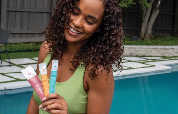 A woman holds 3 NeoraFit sachets while standing by a swimming pool.
