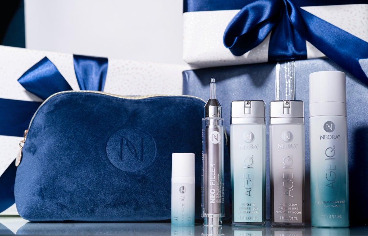 A bundle of Neora skincare products, which include Neo-FILLER, Age IQ Eye Serum, Age IQ Day & Night Creams, and Double-Cleansing Face Wash, surrounded by festive gift boxes and a blue Neora branded velvet bag.