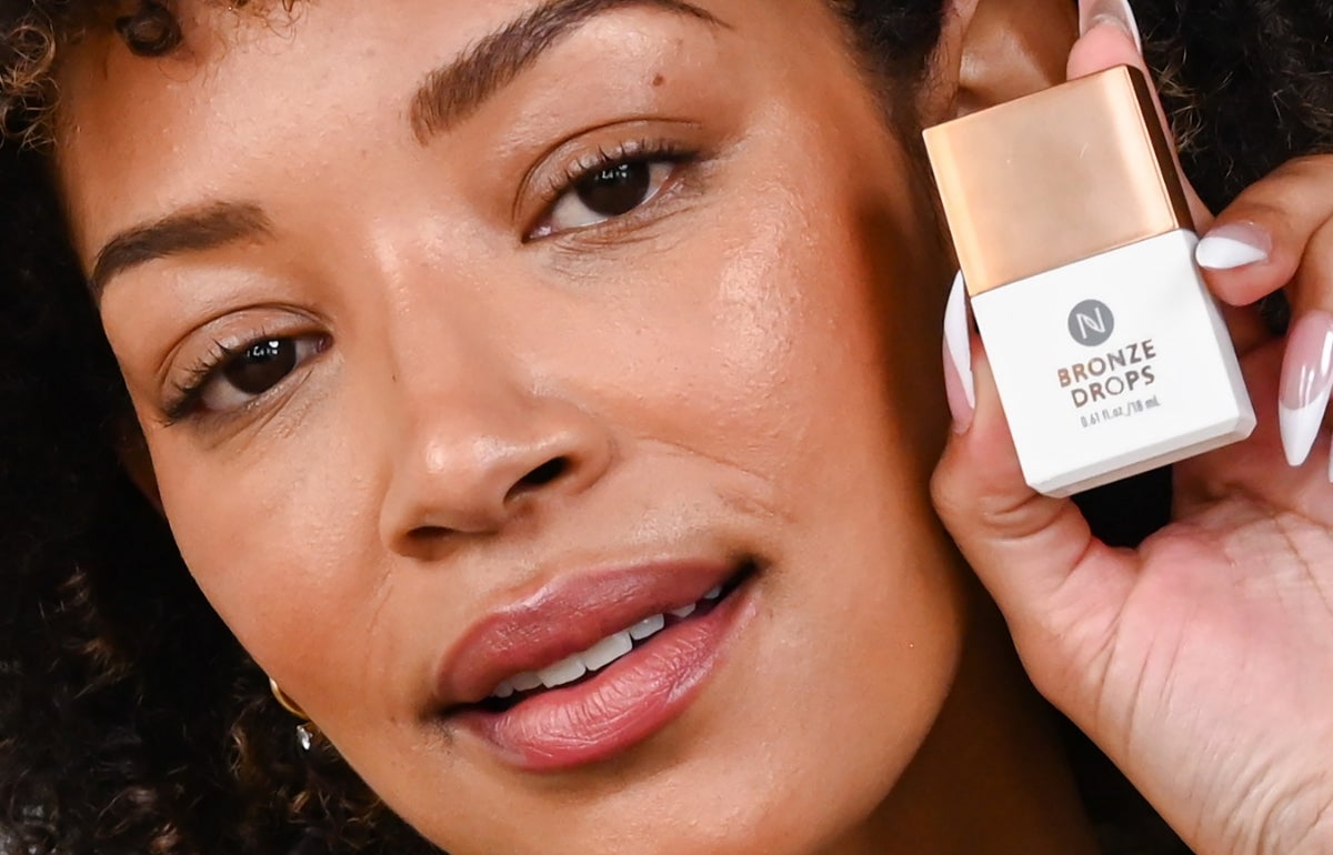 A woman holding a container of Bronze Drops to her face.