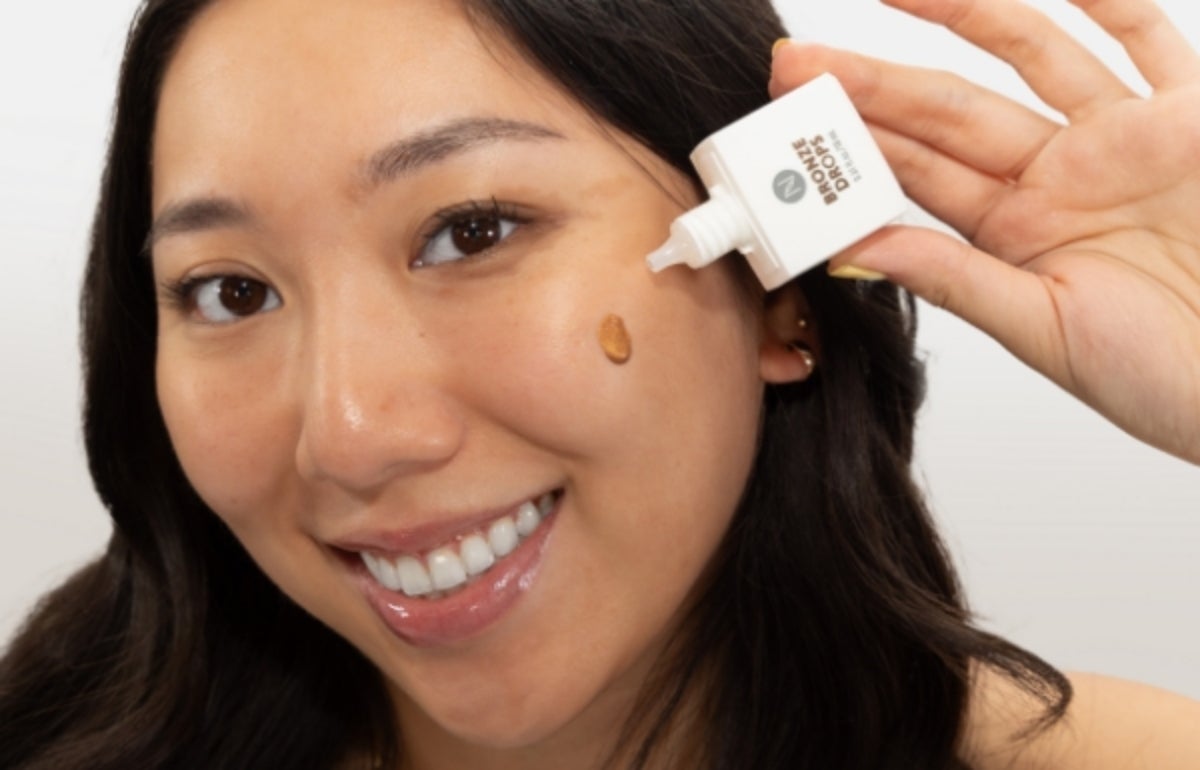 A woman applying a droplet of Bronze Drops to her cheek.