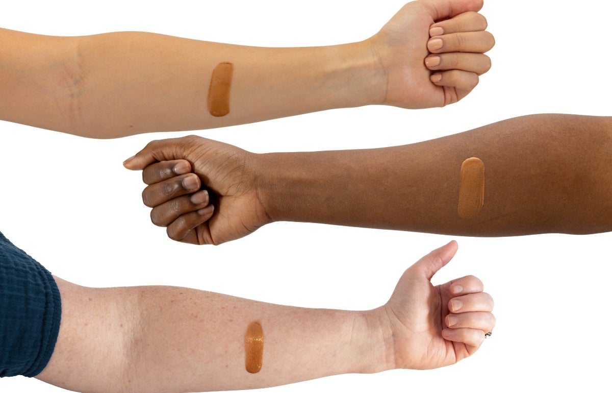 Three arms with various skin tones displaying smears of Bronze Drops on them.