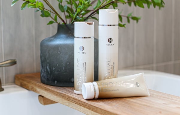 Neora’s ProLuxe Hair Care System featuring ProLuxe Rebalancing Shampoo and Conditioner and ProLuxe Hair Mask sitting on top of a wooden plank on a bath tub