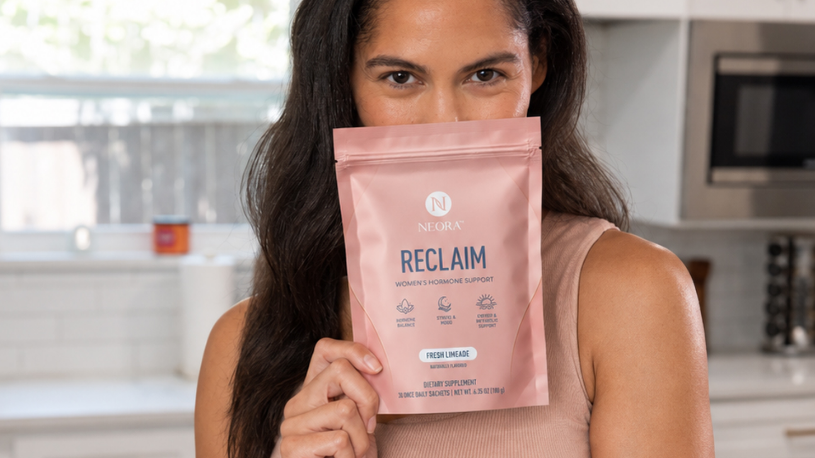 A woman holding a bag of Neora’s RECLAIM to her face.