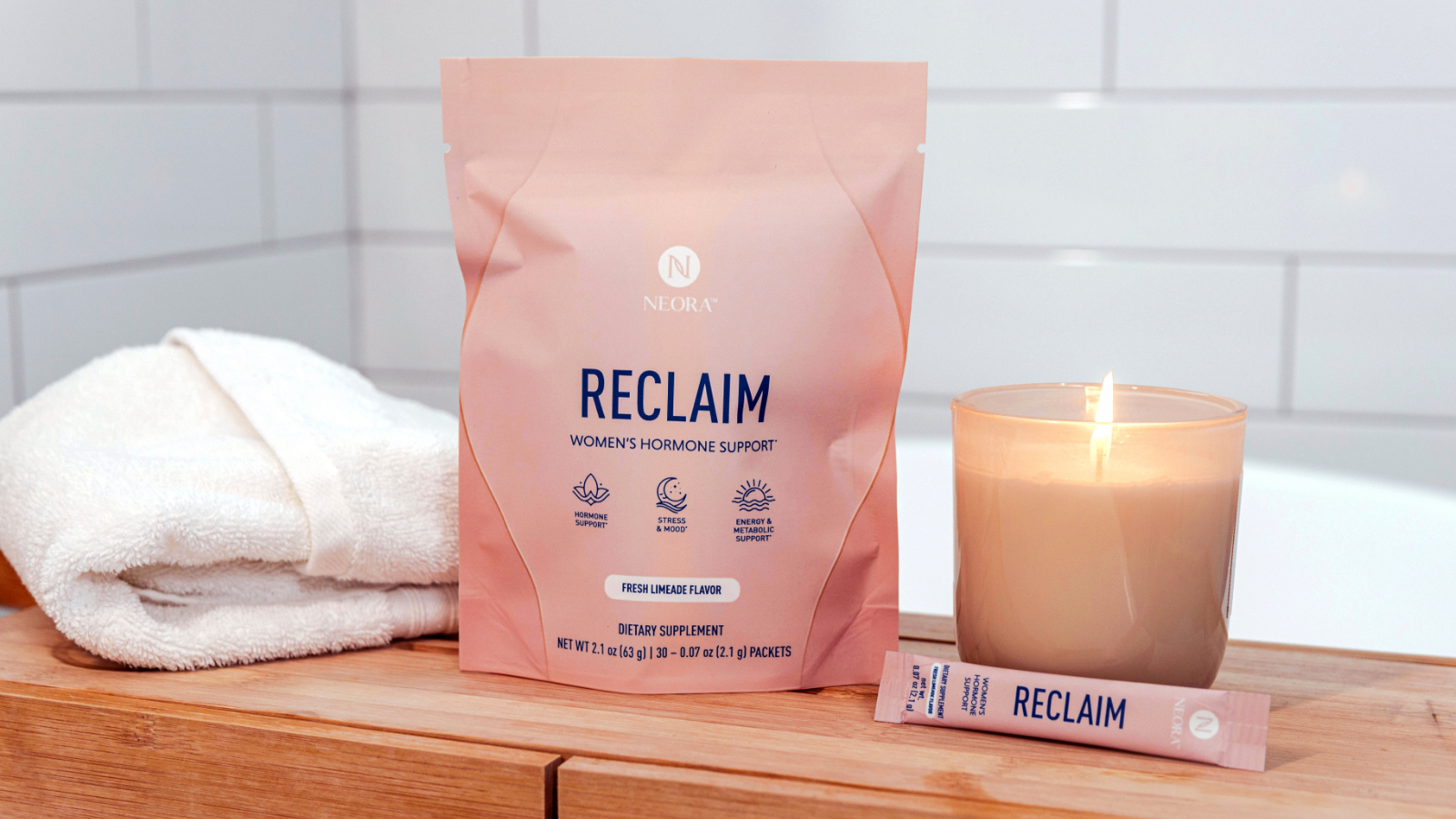 A bag of Neora RECLAIM and product sachet resting next to a lit candle and white towel.