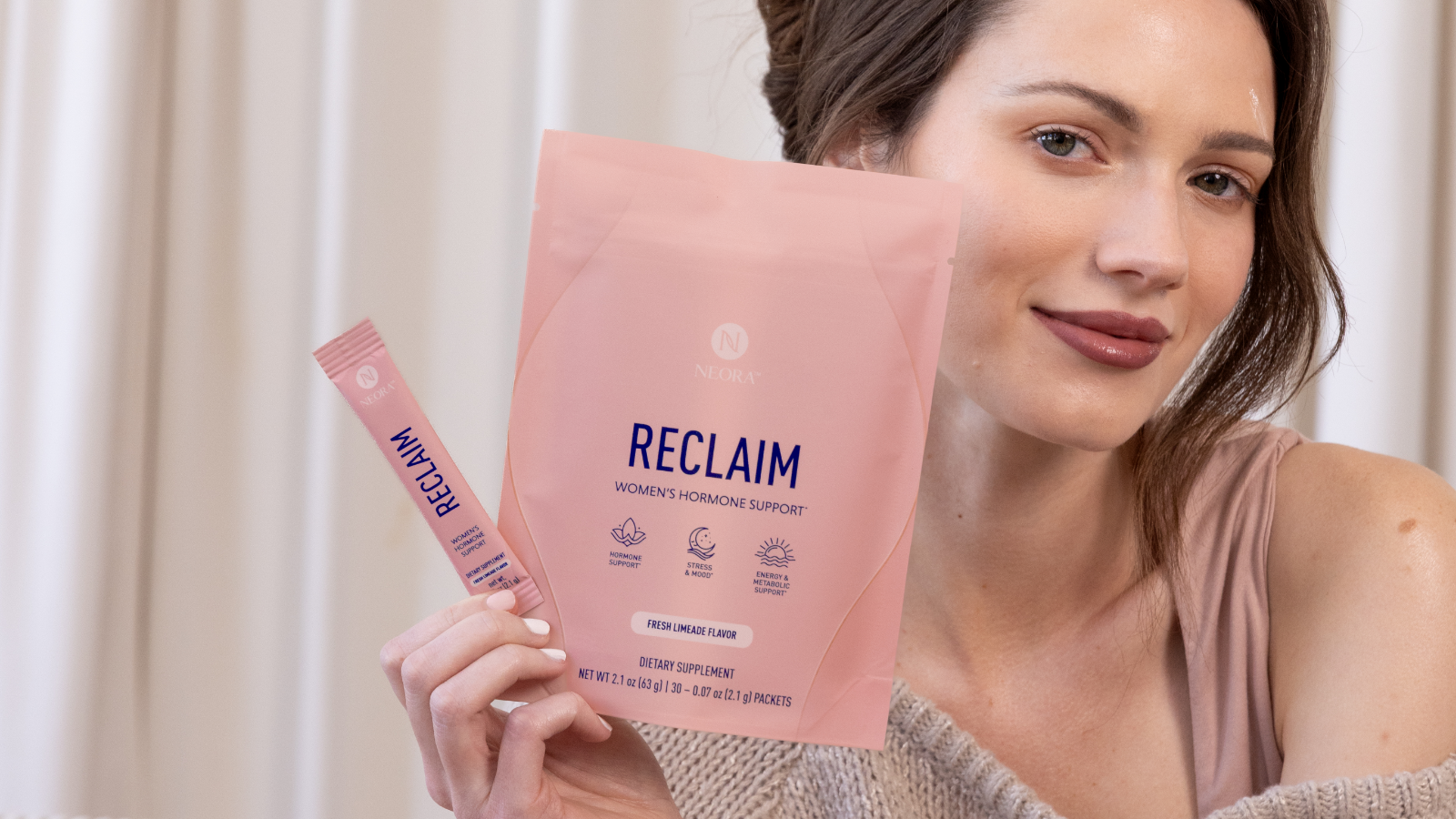 A woman holding a bag of Neora RECLAIM and product sachet next to her face.