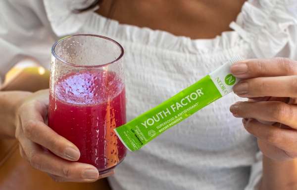 A woman holding up a glass with a mixture of Youth Factor® Superfood & Antioxidant Boost Powder in it.