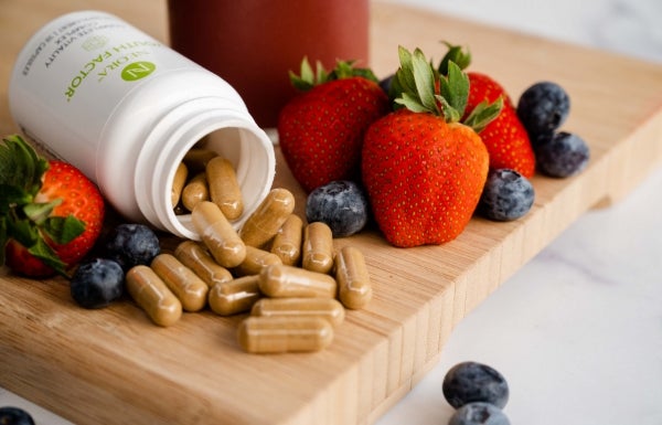 Lifestyle shot of Youth Factor® Complete Vitality Complex spilling out onto a wooden board with berries surrounding it.