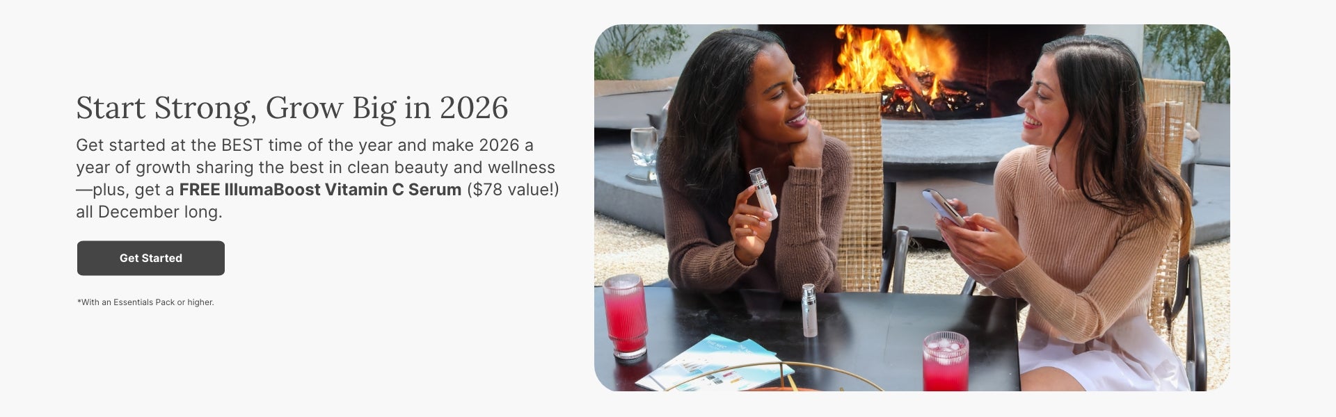 Two women sitting at an outdoor table near a fire pit, smiling and talking. One is holding an IllumaBoost bottle, and the other is holding a phone.