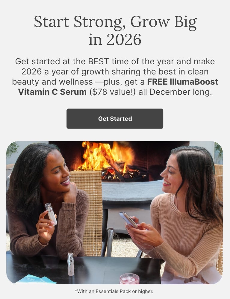 Two women sitting at an outdoor table near a fire pit, smiling and talking. One is holding an IllumaBoost bottle, and the other is holding a phone.