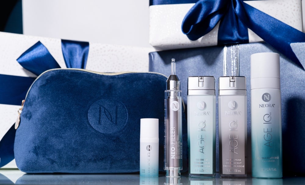 A bundle of Neora skincare products, which include Neo-FILLER, Age IQ Eye Serum, Age IQ Day & Night Creams, and Double-Cleansing Face Wash, surrounded by blue ribbon and a blue Neora branded velvet bag.
