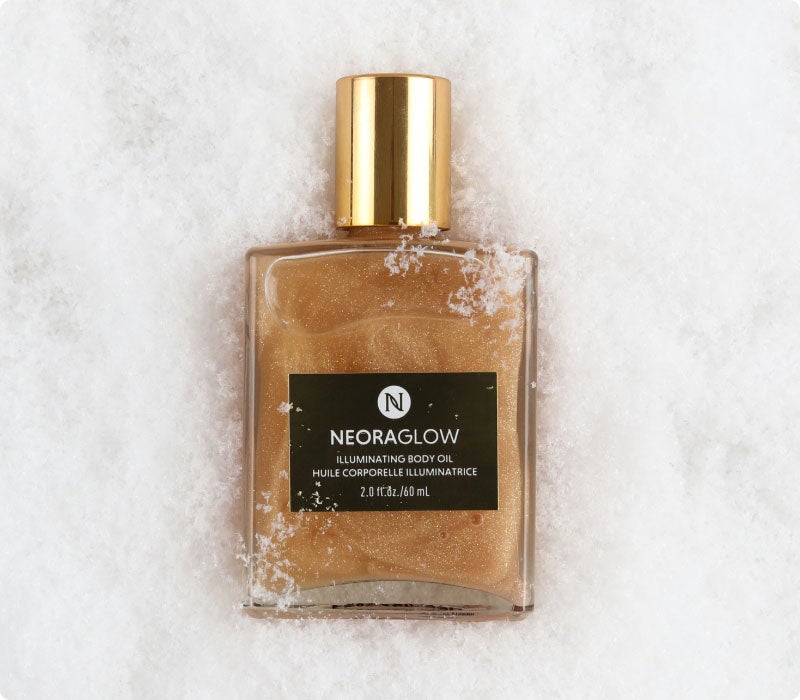Neora’s hottest holiday limited-time must-have, Glisten Up Holiday Body Glow Oil, laying on a bed of snow!