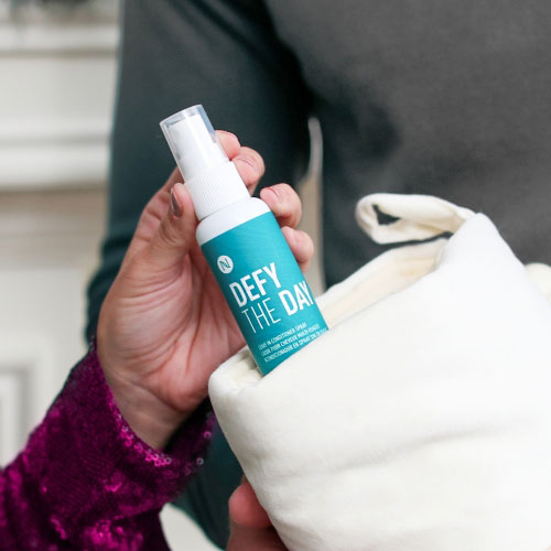 Woman taking Neora’s Holiday Hot List must-have, Defy the Day Leave-in Conditioner Spray, out of a stocking.