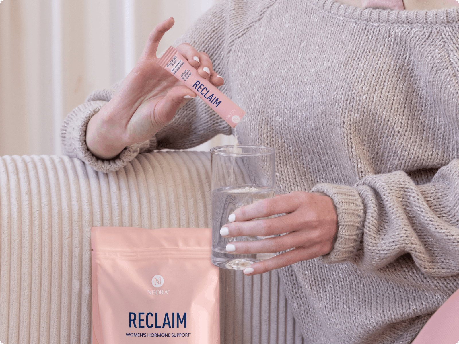 A seated woman on a couch pouring a RECLAIM™ product sachet mixture into a drinking glass.