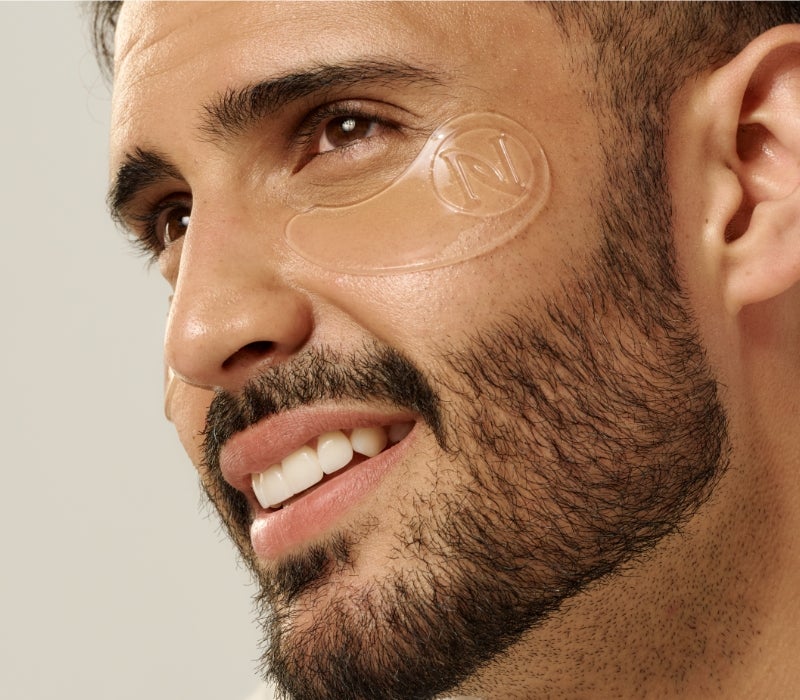 A smiling man with a Neora’s Eye-V™ Hydrogel Patche under his eye.