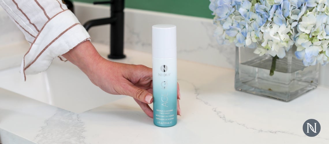 A person holding a bottle of Neora's Double Cleansing Face Wash.