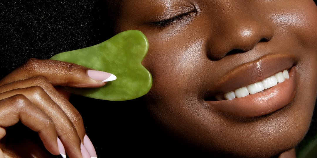 A woman using a green GuaSha on her cheek.