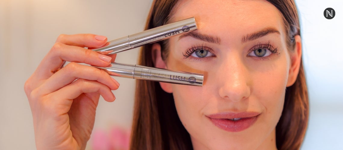A woman holding two tubes of LashLush to her face.