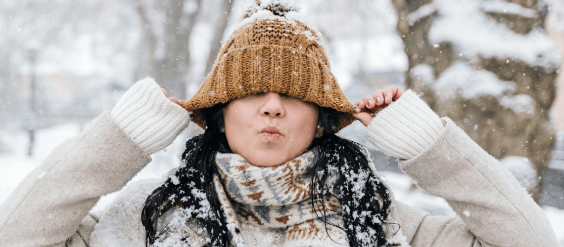 A woman in winter attire pulling on her beanie in a silly manner.