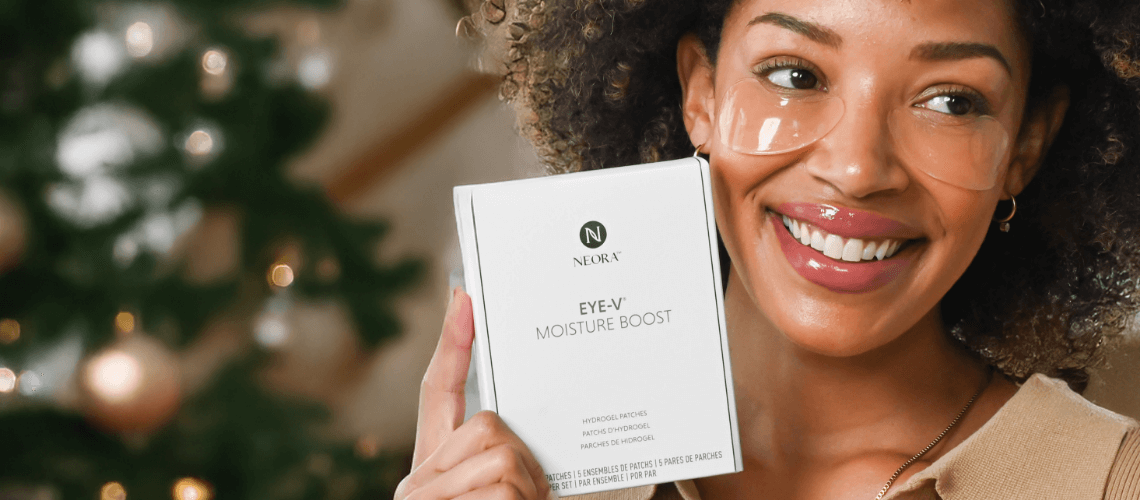 A woman wearing Eye-V Hydrogel Eye Patches while holding a box of packaging up.