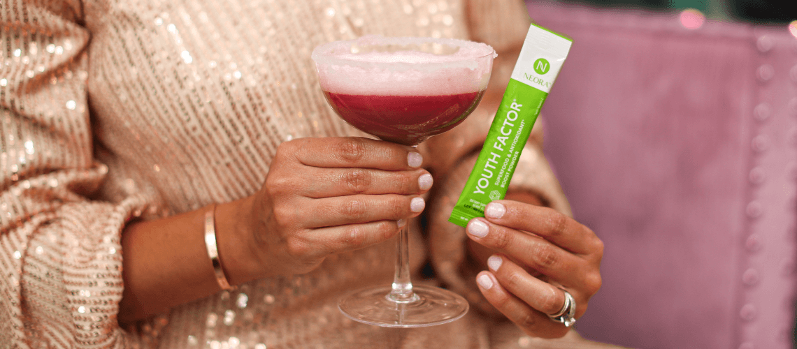 A woman holding a mix drink of Youth Factor while holding a packet up.