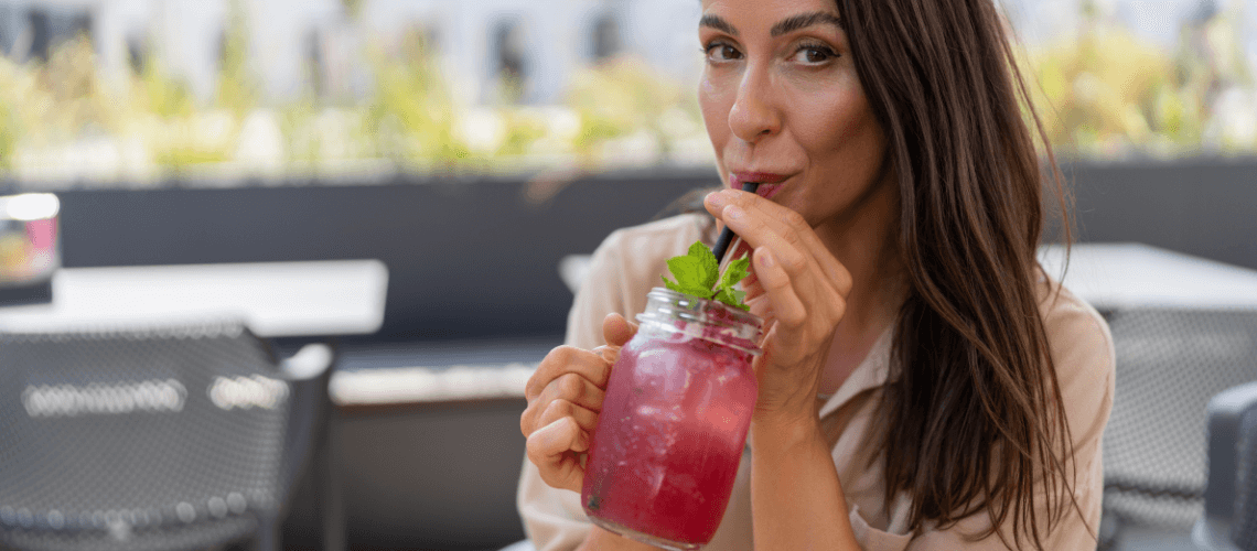 A woman drinking from a mason jar filled with a red liquid.