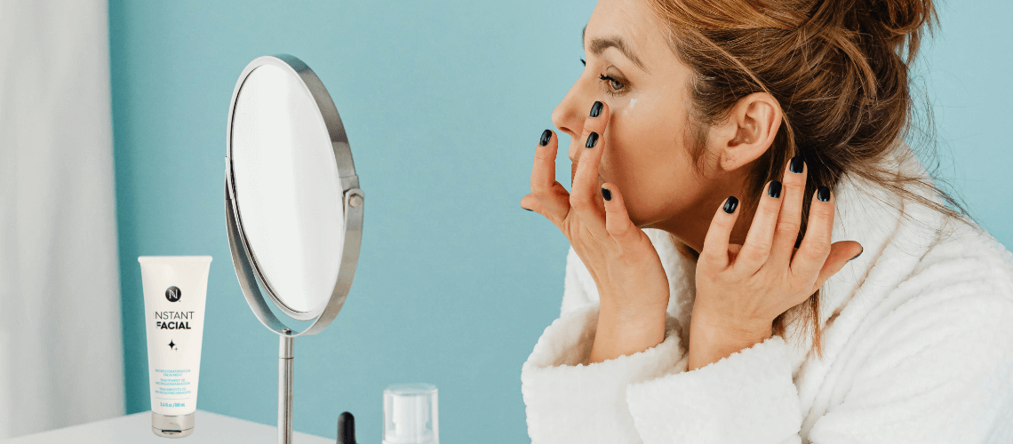 A woman in a bath robe applying eye serum to her undereye.