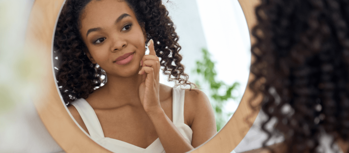 A woman looking in a mirror while applying moisturizer.
