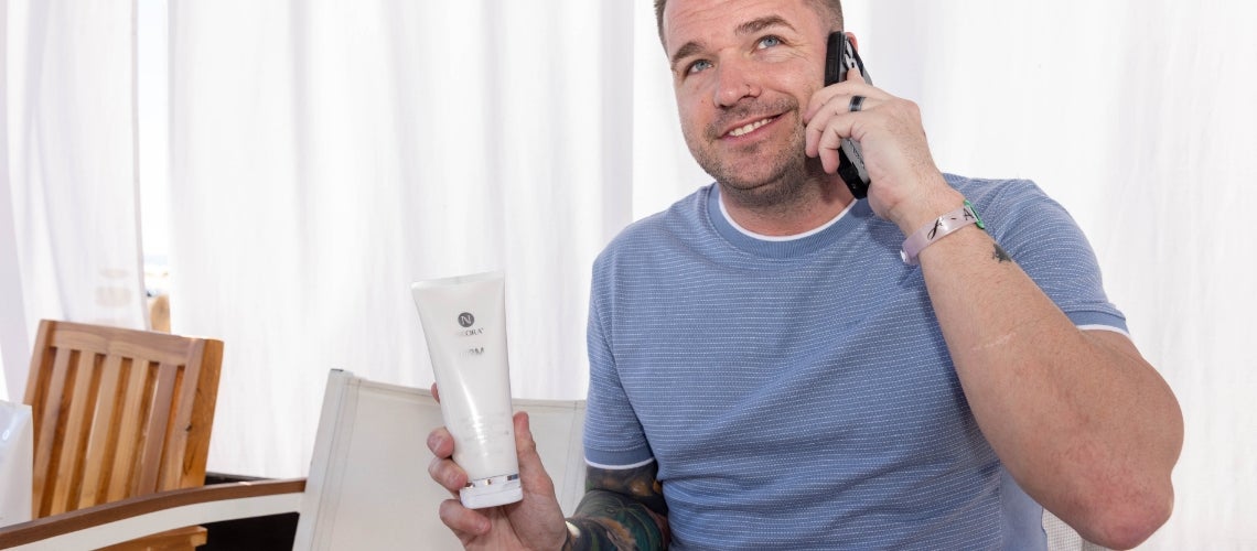 A man talking on the phone while holding a bottle of Firm Contour Cream.