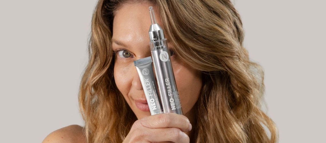 Woman with wavy hair holds two silver Neo-Filler cosmetic tubes up to her face, promote skincare product.
