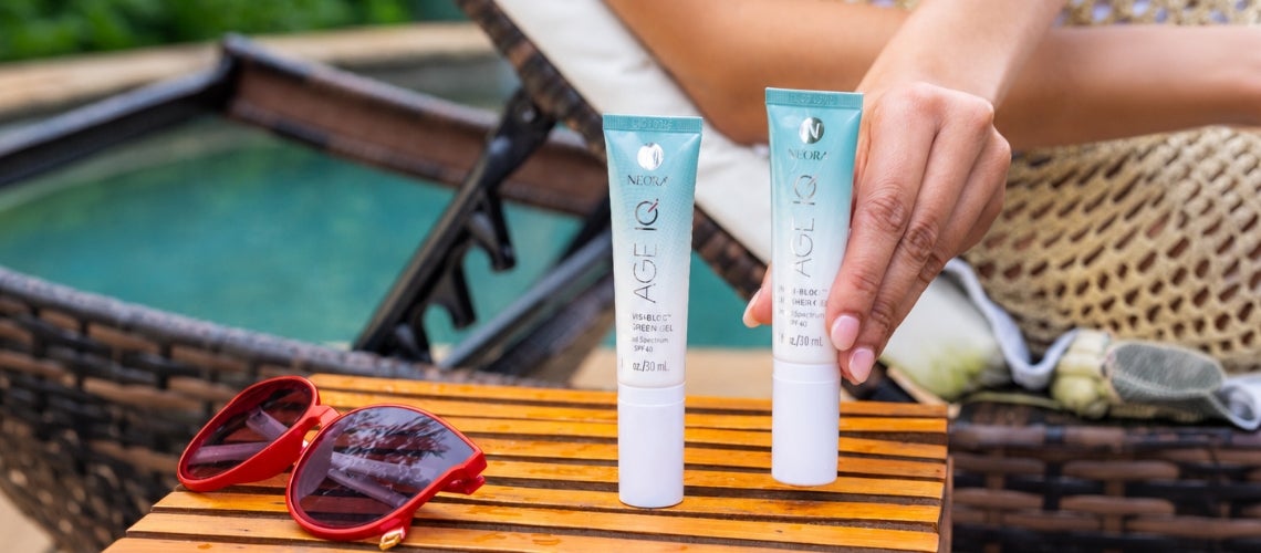 Two blue-and-white cosmetic tubes labeled Age Gel on a wooden table by a pool, with red sunglasses nearby.