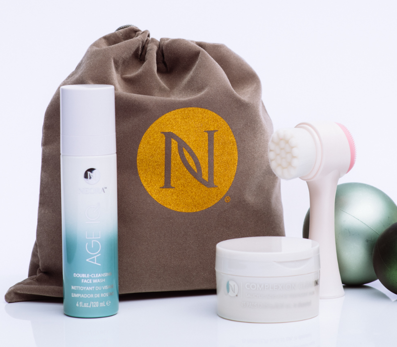 Neora’s hottest holiday must-have, the Clear Skin Set, which includes Age IQ Double-Cleansing Face Wash, Complexion Treatment Pads and FREE Dual-Action Facial Cleansing Brush surrounded by Christmas ornaments.