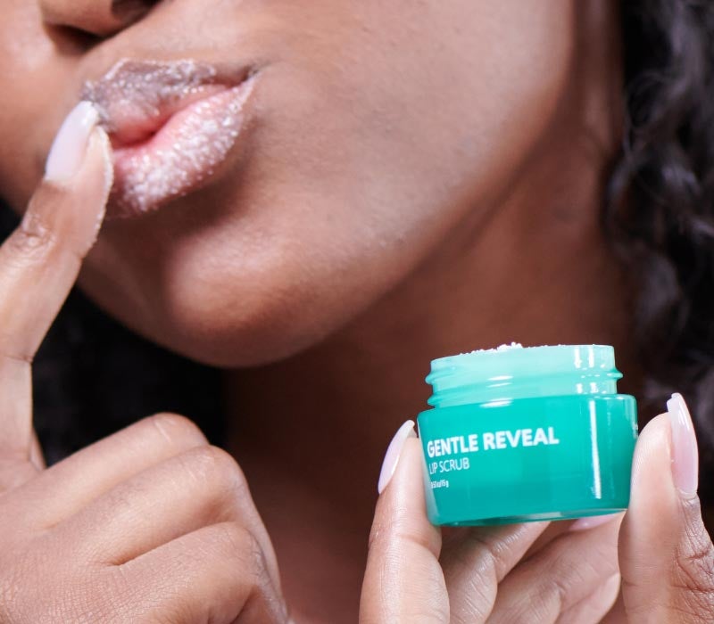 Mujer poniéndose el producto Hot List de Neora, Gentle Reveal Exfoliante Labial, en los labios con los dedos
